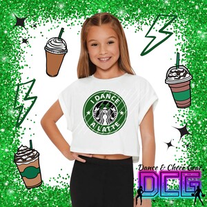 May include: A white crop top with a green and white graphic of a coffee cup with the text "I Dance A Latte". The model is wearing black leggings and has a green glitter background.