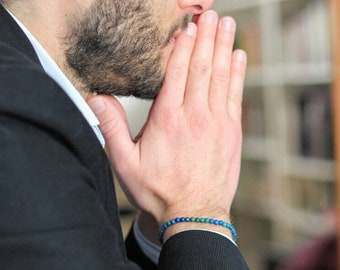 May include: A beaded bracelet featuring small, round, vibrant blue and green stones worn on the wrist. The bracelet consists of a single strand of polished, uniform beads that encircle the wrist, showcasing a consistent color pattern throughout.
