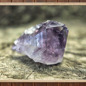 Puede incluir: Un gran cristal de amatista púrpura con una punta puntiaguda, descansando sobre un trozo de madera desgastada.
