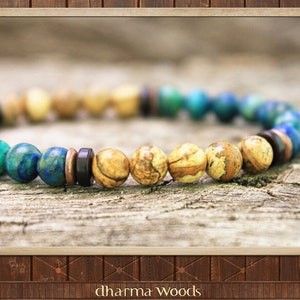 May include: A beaded bracelet featuring a sequence of round beads in shades of blue, green, tan, and brown. The design includes smooth, polished stone beads interspersed with small, dark, flat circular spacers, creating a varied pattern.