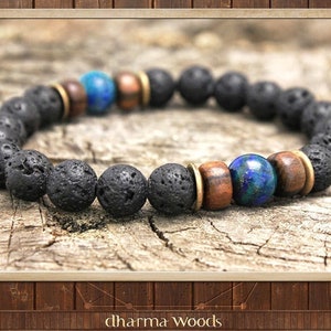 May include: A beaded bracelet featuring porous black lava stone beads, smooth brown wooden beads, metallic gold-toned spacers, and two polished blue and green azurite beads. The text "dharma WOODS" is printed in white at the bottom of the image.