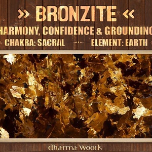May include: Close-up of a golden brown bronzite crystal. The text ">>> BRONZITE <<< HARMONY, CONFIDENCE & GROUNDING CHAKRA: SACRAL ELEMENT: EARTH dharma woods" is visible at the top and bottom of the image.