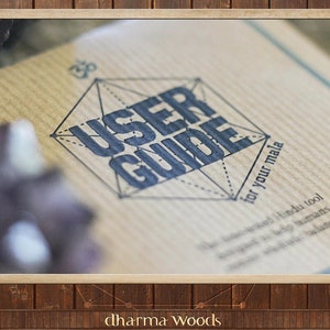May include: A tan paper user guide for a mala featuring a dark blue geometric design with the text USER GUIDE for your mala printed in the centre. An Om symbol is positioned above the geometric shape, and additional text is printed below.
