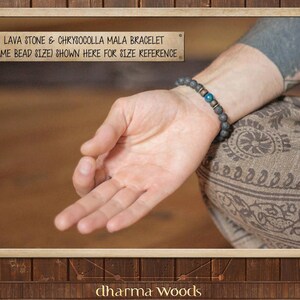 May include: A person wearing a black lava stone and chrysocolla mala bracelet with gold accents. The bracelet is shown on a person's wrist to demonstrate the size. The text "LAVA STONE & CHRYSOCOLLA MALA BRACELET (SAME BEAD SIZE) SHOWN HERE FOR SIZE REFERENCE" is displayed above the image. The text "dharma Woods" is displayed below the image.
