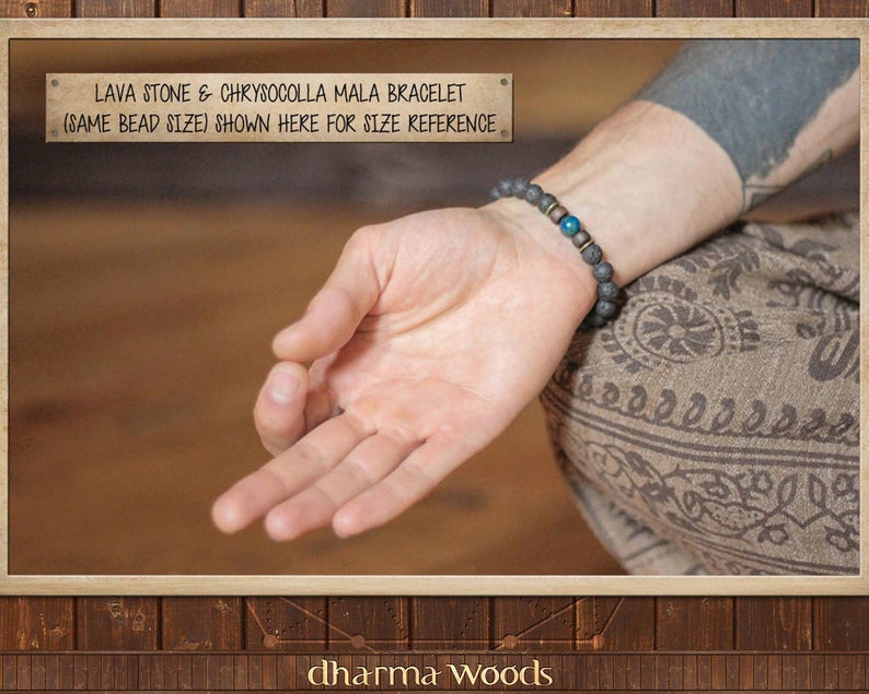 May include: A person wearing a black lava stone and chrysocolla mala bracelet with gold accents. The bracelet is shown on a person's wrist to demonstrate the size. The text "LAVA STONE & CHRYSOCOLLA MALA BRACELET (SAME BEAD SIZE) SHOWN HERE FOR SIZE REFERENCE" is displayed above the image. The text "dharma Woods" is displayed below the image.
