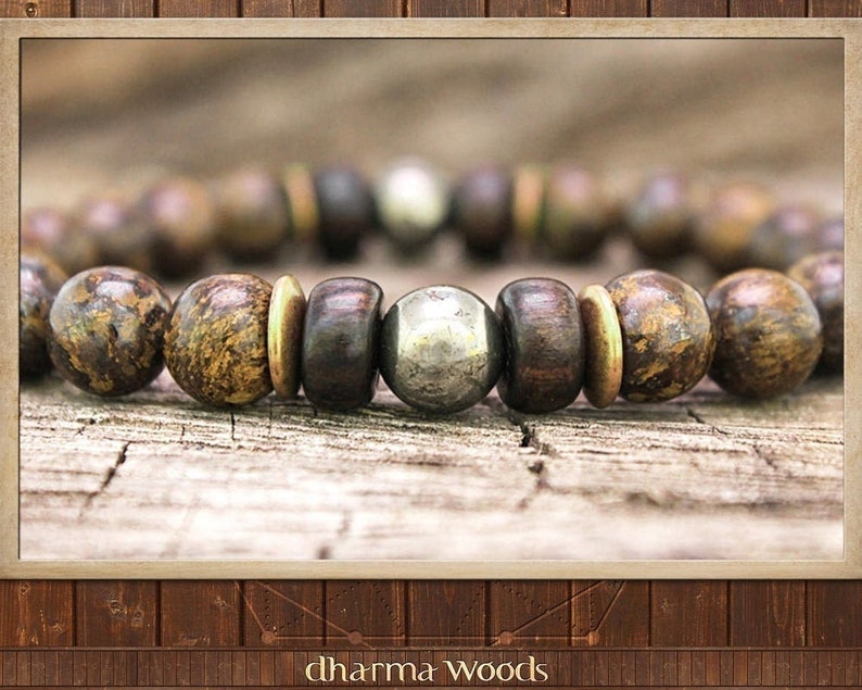 May include: A brown and gold beaded bracelet with a silver metal bead in the center. The bracelet is on a wooden surface.