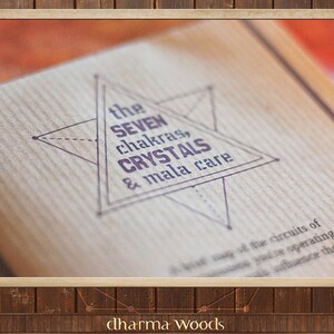 May include: A light brown textured surface featuring a dark purple printed design of a six-pointed star containing the text: the SEVEN chakras, CRYSTALS & mala care. Below the star, additional text reads: a true map of the circuits of.