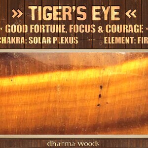 May include: A polished Tiger's Eye gemstone with golden-brown bands and chatoyant luster. The text reads: TIGER'S EYE, GOOD FORTUNE, FOCUS & COURAGE, CHAKRA: SOLAR PLEXUS, ELEMENT: FIRE, and dharma WOODS, set against a dark brown wooden background.