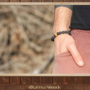 May include: A beaded bracelet featuring dark, porous black lava stone beads and a single textured, spherical gold-toned accent bead. The bracelet is strung on an elastic cord and worn around the wrist, showcasing a contrast between the matte black stones and the metallic gold bead.