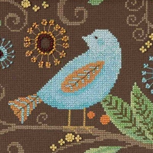 May include: Cross-stitch artwork of a blue bird with orange and brown accents perched on a branch. The bird is set against a brown background with floral and leaf patterns. The artwork is framed in a brown wooden frame.