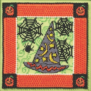 May include: A cross-stitch Halloween design featuring a witch's hat decorated with yellow moons and stars, spiderwebs, and a black spider. The design is framed with orange and green borders, and includes jack-o'-lanterns in each corner.