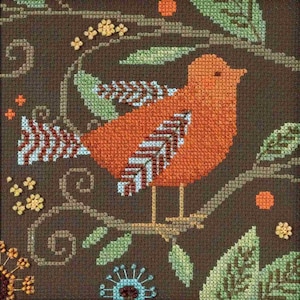 May include: Cross-stitch design featuring an orange bird perched on a branch. The bird has detailed wing patterns in white, brown, and blue. The background is a dark brown with green leaves, yellow flowers, and orange berries.