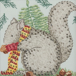 May include: A cross-stitch design of a grey squirrel wearing a red and yellow scarf, with green pine needles and small pine cones. The squirrel is sitting on green grass, with a light background.