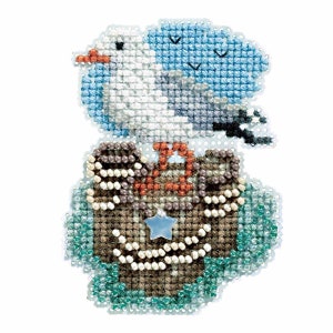 May include: A cross-stitch design featuring a blue and white bird with an orange beak, perched atop a brown chest. The chest has a blue star-shaped charm. The design includes small black birds in the sky and is surrounded by a teal border.