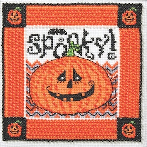 May include: Cross-stitch Halloween design featuring an orange pumpkin with a smiling face, the word "Spooky!" and a bat. The design is framed in orange and black with pumpkin corner accents. The background is white.