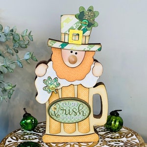 May include: A wooden leprechaun figurine holding a beer mug with the text "I'll be Irish" and a shamrock design. The figurine is on a tiered wooden tray with green shamrock decorations.