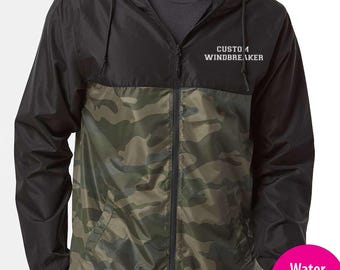 May include: A black and camouflage windbreaker jacket with a zipper closure and a hood. The jacket has the text "Custom Windbreaker" embroidered on the front. The jacket is water resistant and available in 14 colors.