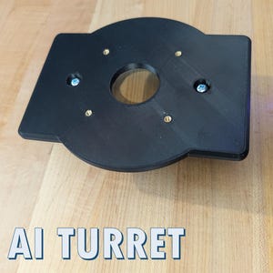 May include: A black, geometric component with a central circular opening and several smaller holes, secured with brass and silver hardware. The text "AI TURRET" is displayed in a blue and white font at the bottom of the image. The component is on a wooden surface.