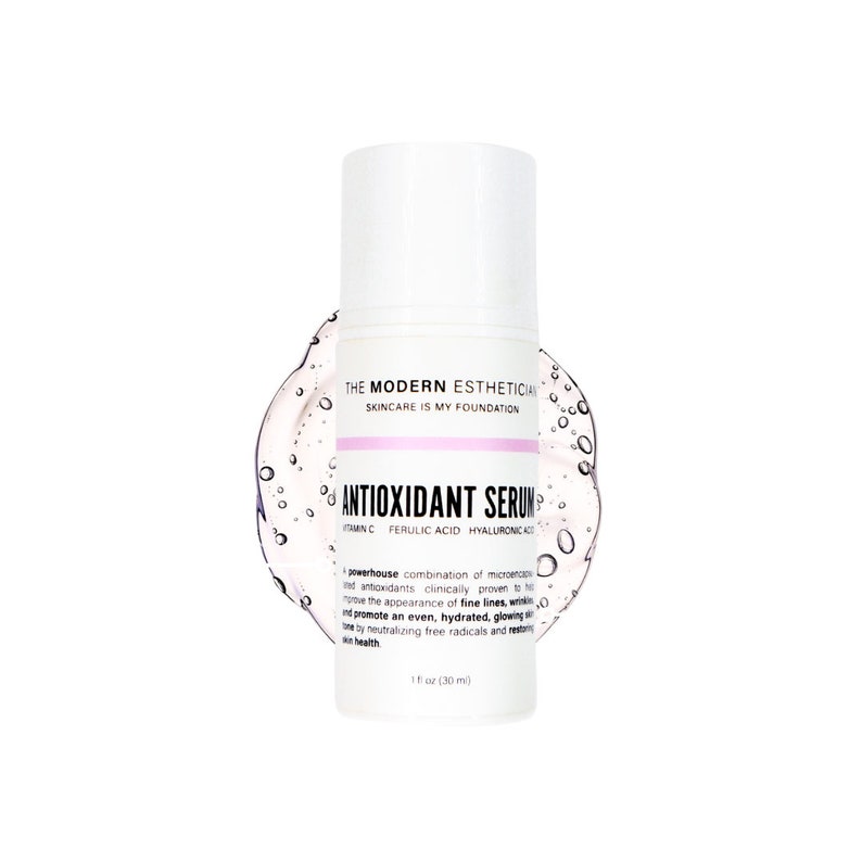 May include: A white bottle with a pink label that says "ANTIOXIDANT SERUM" with the ingredients listed below. The bottle is sitting on a white background with a clear liquid surrounding it.