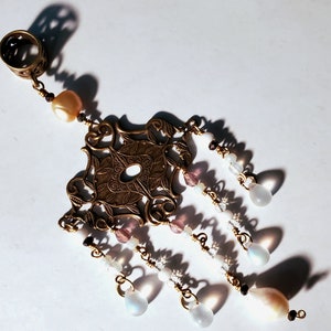 May include: A gold-toned pendant with a filigree design and multiple strands of beads. The beads are white, pink, and iridescent.