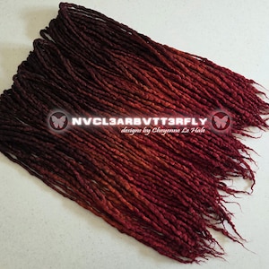 Op de afbeelding: Een bundel handgemaakte dreadlocks in een verloop van donkerbruin naar rood-oranje tinten. De dreads zijn dik en getextureerd, met een natuurlijke, licht gerafelde uitstraling. De afbeelding bevat de tekst "NVCL3ARBVTT3RFLY designs by Cheyenne Le Hale".