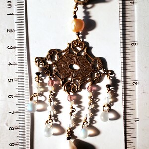 May include: A gold filigree pendant with a pearl and iridescent glass drops hanging from it. The pendant is attached to a ring that can be used to hang it from a chain or bracelet.