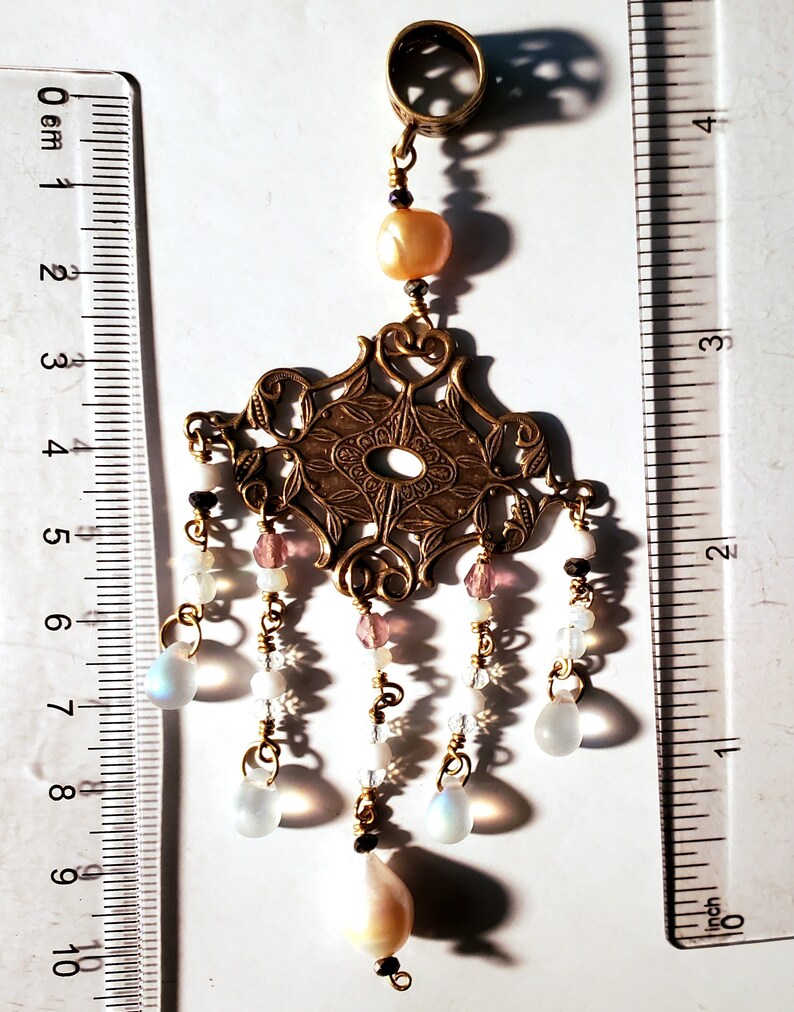 May include: A gold filigree pendant with a pearl and iridescent glass drops hanging from it. The pendant is attached to a ring that can be used to hang it from a chain or bracelet.