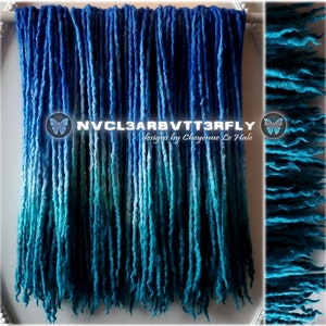 Könnte beinhalten: Ein Satz blauer und türkisfarbener Ombre-Dreadlocks aus synthetischem Material mit Glitzer. Die Dreadlocks hängen an einer weißen Oberfläche. Der Text "NVCL3ARBVTTR3FLY designs by Cheyenne Le Hale" ist auf dem Bild zu sehen.
