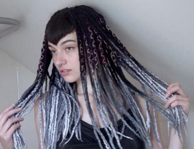 May include: A set of synthetic dreadlocks featuring a gradient color scheme that transitions from deep black at the roots to shades of charcoal gray and light silver at the tips. The individual strands are textured with a braided or wrapped pattern.
