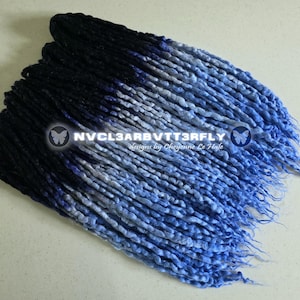 May include: A bundle of synthetic dreadlocks in a gradient of colors, transitioning from black to shades of blue and white. The text "NVCL3ARBVTT3RFLY designs by Cheyenne Le Hale" is visible.