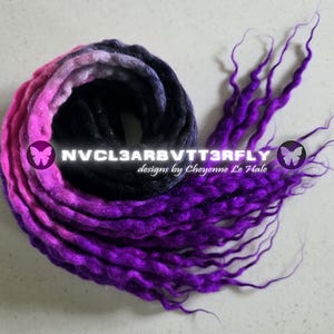 Puede incluir: Un conjunto de rastas moradas, rosas y negras. Las rastas están dispuestas en espiral, con los extremos de las rastas extendiéndose. El texto "NVCL3ARBVTT3RFLY designs by Cheyenne Le Hale" es visible.