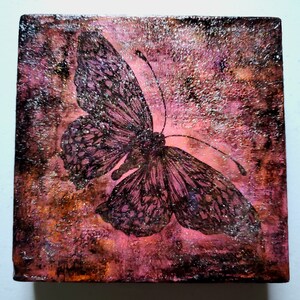 Puede incluir: Una silueta de mariposa negra sobre un fondo texturizado rosa y marrón con acentos de purpurina.