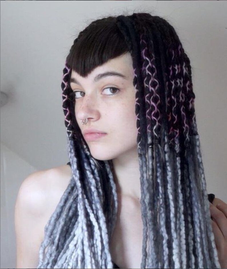 May include: A set of long hair extensions featuring black roots with pink and white interwoven thread detailing, transitioning into textured grey and white yarn-like strands. The extensions are styled with straight dark bangs and a septum ring.
