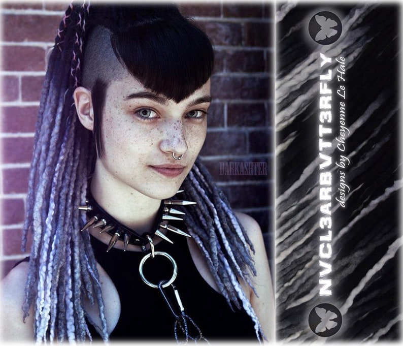May include: A black choker featuring silver-toned metal spikes and a central O-ring with a carabiner attachment. The accessory is worn with long, textured grey and black synthetic dreadlocks and a septum piercing, with text reading NVCL3ARBVT3RFLY.