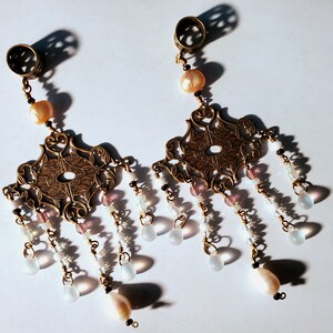 May include: A pair of gold-toned earrings with intricate filigree designs and dangling white and pink beads.