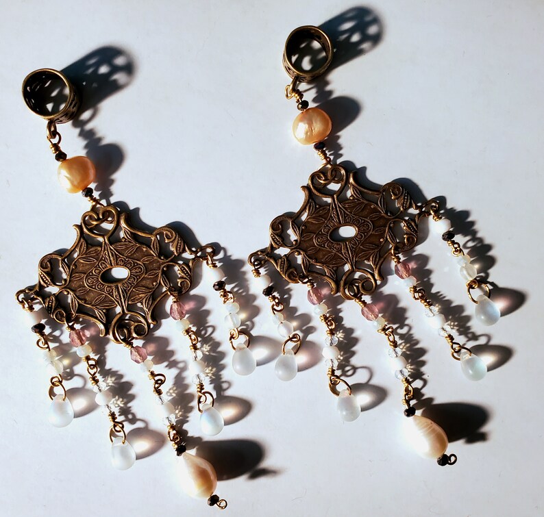 May include: A pair of gold-toned earrings with intricate filigree designs and dangling white and pink beads.