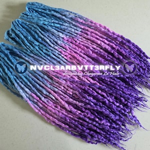 May include: A set of blue, purple, and pink dreadlocks. The dreadlocks are arranged in a layered pattern, with the colors blending from blue to purple. The text "NVCL3ARBVTT3RFLY designs by Cheyenne Le Hale" is visible.