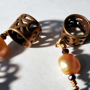 May include: A gold necklace with two ornate metal spacers and two pearlescent beads. The spacers have a filigree design.