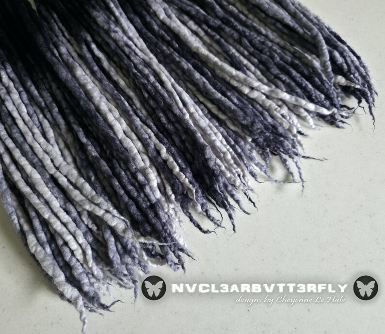 May include: A collection of long, thin, twisted synthetic hair extensions featuring a gradient color transition from deep black at the top to a light grey and white at the ends. The text NVCL3ARBVTT3RFLY designs by Cheyenne Le Hale is visible.