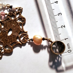 May include: A gold-toned pendant necklace with a filigree design and a pearl bead. The necklace is 1 cm long.