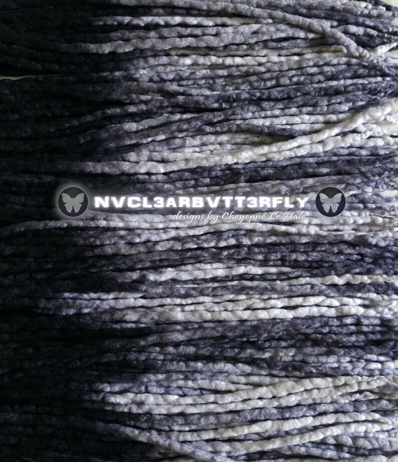 May include: A collection of long, thin, braided hair extensions featuring a gradient color pattern that transitions from deep black to charcoal gray and bright white. The text NVCL3ARBVTT3RFLY designs by Chyenne Le Hale is centered.