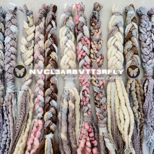 Puede incluir: Una colección de doce trenzas de arte textil verticales en tonos crema, marrón, rosa y gris. Cada trenza presenta texturas variadas, incluyendo lana gruesa, encaje y cinta, con flecos sueltos en la parte inferior. Texto: NVCL3ARBVTT3RFLY designs by Cheyenne Le Hale.