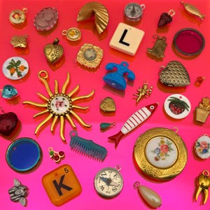 May include: A collection of assorted charms including a gold sun, a white tile with the letter L, an orange tile with the letter K, a blue telephone, a red and white fish, a floral locket, compasses, hearts, and various miniature decorative items.