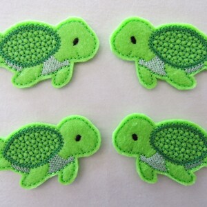 May include: Four green felt turtle appliques with white stitching. Each turtle has a green shell with a textured pattern and a white underbelly.