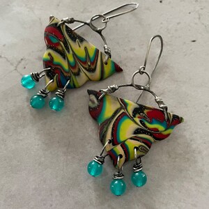 May include: A pair of colorful, abstract, swirl-patterned earrings with silver wire accents and turquoise beads dangling from the bottom.