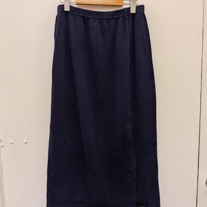 May include: A solid navy blue midi-length skirt featuring an elasticated waistband and a straight silhouette. The skirt is constructed from a soft, fleece-like fabric and includes a vertical slit detail along the lower right side of the front panel.