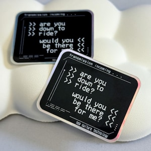 May include: Two black and silver holographic stickers with a retro computer screen design. The text on the stickers reads "Transmission incoming... are you down to ride? would you be there for me?"