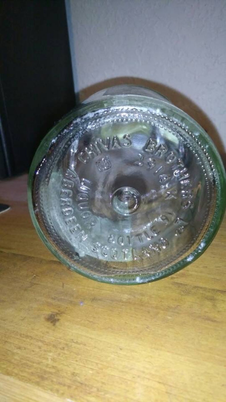 Op de afbeelding: Close-up van de bodem van een heldere glazen fles met een etiket met de tekst "Chivas Brothers" en "Scotch Whisky Bottled in Scotland".