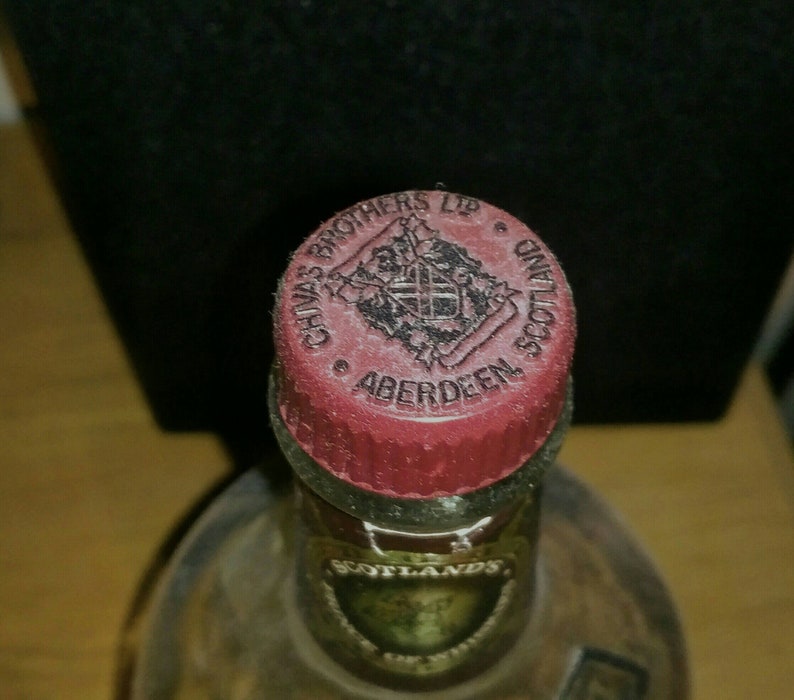 Op de afbeelding: Close-up van een rode dop met een zwart-wit logo met de tekst "Chivas Brothers Ltd. Aberdeen Scotland".