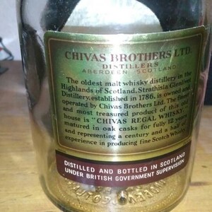 Op de afbeelding: Een close-up van een etiket van een Chivas Brothers Ltd. Scotch whisky-fles. Het etiket is goudkleurig met zwarte tekst en vermeldt dat de distilleerderij de oudste malt whisky-distilleerderij in de Schotse Hooglanden is. Het etiket vermeldt ook dat de distilleerderij in 1786 werd opgericht en eigendom is van en wordt ge&euml;xploiteerd door Chivas Brothers Ltd. Het etiket vermeldt ook dat het beste en meest gewaardeerde product van dit oude huis "Chivas Regal Whisky" is en dat het 12 jaar lang in eiken vaten wordt gerijpt.